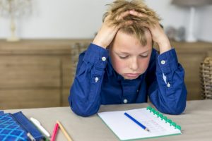 Image showing a schoolboy struggling with his work, holding his hands in his hair on a page for the benefits of Maths tuition