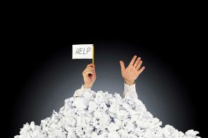 Image showing a pair of hands appearing from a mountain of Maths papers with a white flag having the word HELP written on it on a page for the benefits of Maths tuition Easter Maths Revision Booster Sessions