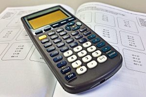 Image showing a calculator on top of a work book of Maths questions on a page for the benefits of Maths tuition